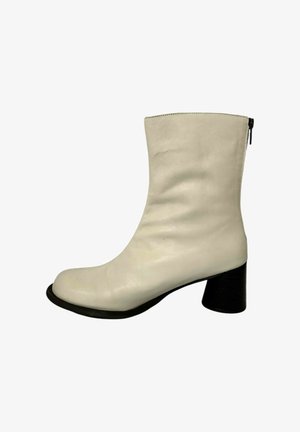 Botín de cuero blanco hasta el tobillo, con punta redonda, textura suave y un tacón grueso negro. Presenta un detalle de cremallera lateral para facilitar el uso.