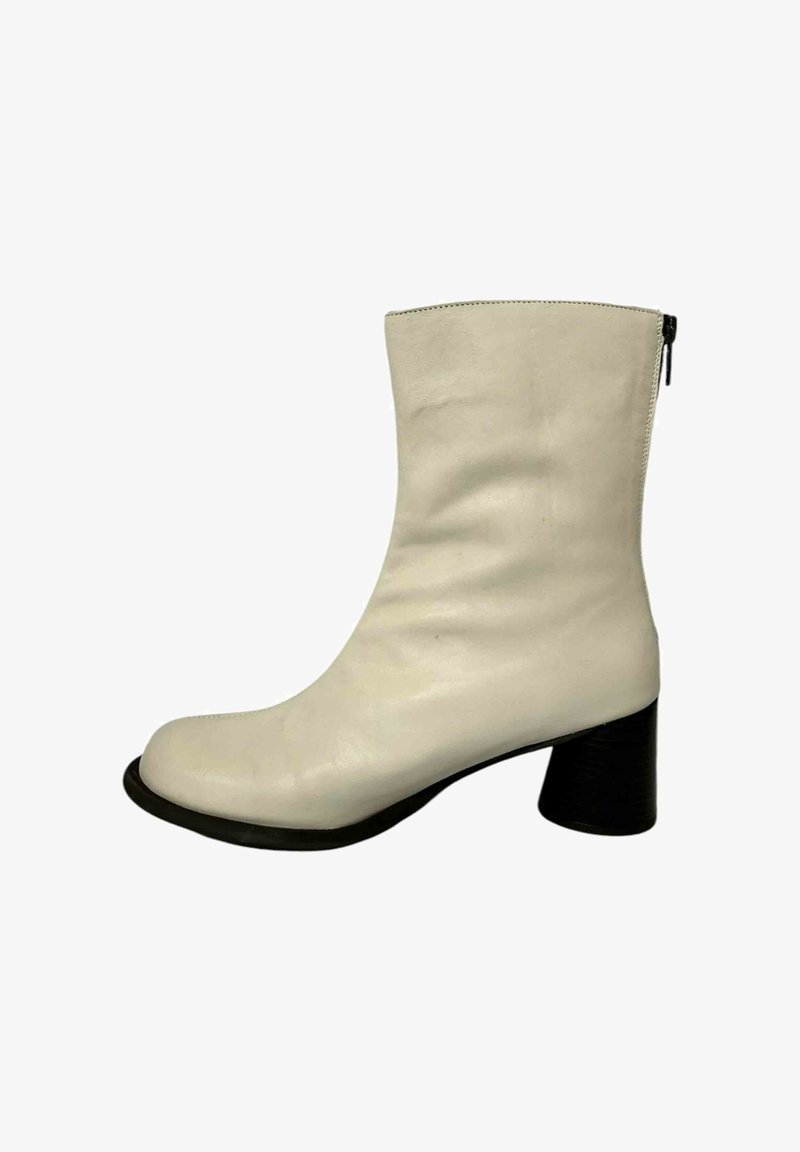 Botín de cuero blanco hasta el tobillo, con punta redonda, textura suave y un tacón grueso negro. Presenta un detalle de cremallera lateral para facilitar el uso.