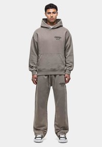 Hoodie en bijpassende joggingbroek in gedempt grijs. De stoffen zijn zacht, met grote voorkant zak en bedrukte tekstdetails. Casual pasvorm.