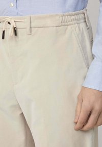 Pantalones de pana beige con una cinturilla elástica y cordón. Presentan bolsillos laterales y una textura suave. Costuras detalladas a lo largo de las costuras.