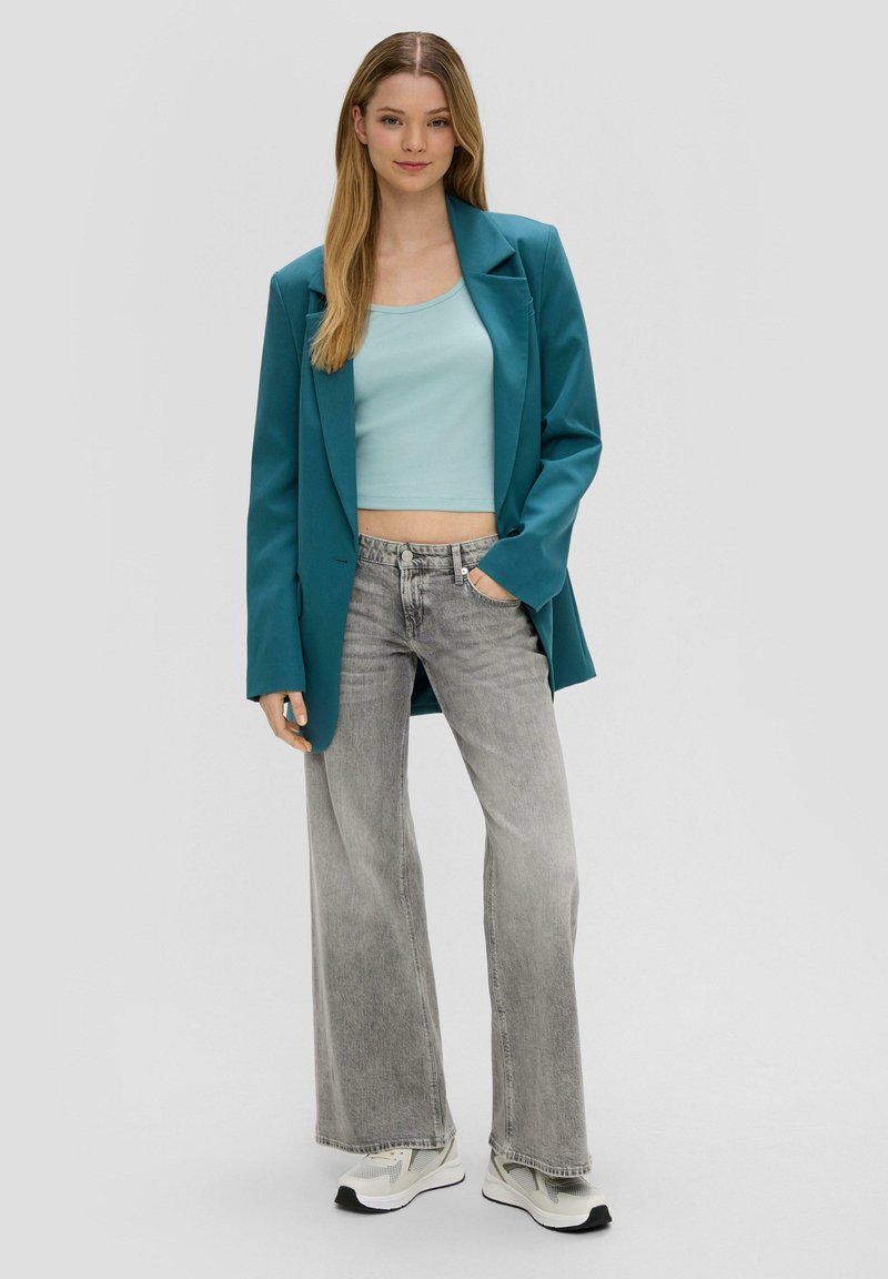 Een teal blazer over een lichtblauw ribgebreid crop top, gecombineerd met wijde, vervaagde grijze jeans en witte sneakers met zwarte accenten.