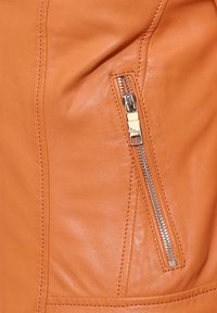 Orangene Lederjacke mit einer Reißverschlusstasche und silbernen Beschlägen, glatter Textur und feiner Naht entlang der Nähte.