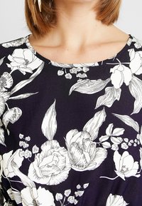 Floral top in dark navy with white botanical prints. Features a rounded neckline and short sleeves, made from a smooth fabric.