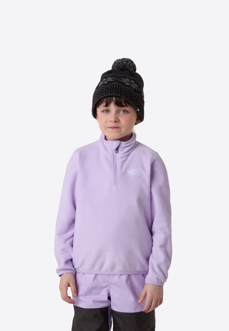 Polarowy sweter w jasnym lawendowym kolorze z kołnierzem na zamek, w połączeniu z ciemną, wzorzystą dzianą czapką. Dziecko nosi spodnie narciarskie w dopasowanych kolorach.