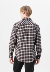 Brown and white checkered shirt with a classic collar, long sleeves, and button cuffs, featuring a curved hem and textured fabric.