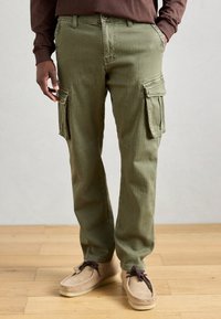 Oliven grønne cargo bukser med side lommer, lige ben design og struktureret stof, parret med lyse beige mokkasiner.