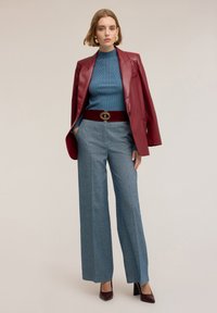 Sacou din piele roșie, pulover tec ribetat, pantaloni largi gri și o curea burgundy cu accesorii aurii. Pantofii cu toc completează ținuta.