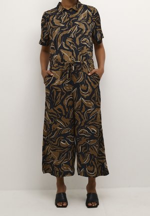 Vrouw in een zwart en bruin jumpsuit met abstract patroon, korte mouwen, een kraag, knopen aan de voorkant en zijzakken.