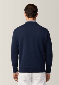 Felpa blu navy con polsini e orlo a costine, caratterizzata da un collo a giro ed una superficie liscia. Camicia a quadri bianca visibile al colletto.