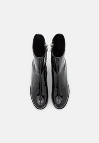 Une paire de bottines noires brillantes avec des zippers vues de dessus sur un fond blanc.