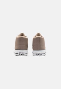 Beżowe płócienne tenisówki niskie z białą gumową podeszwą, z czarnymi akcentami w paski i logo "Converse All Star" na pięcie.