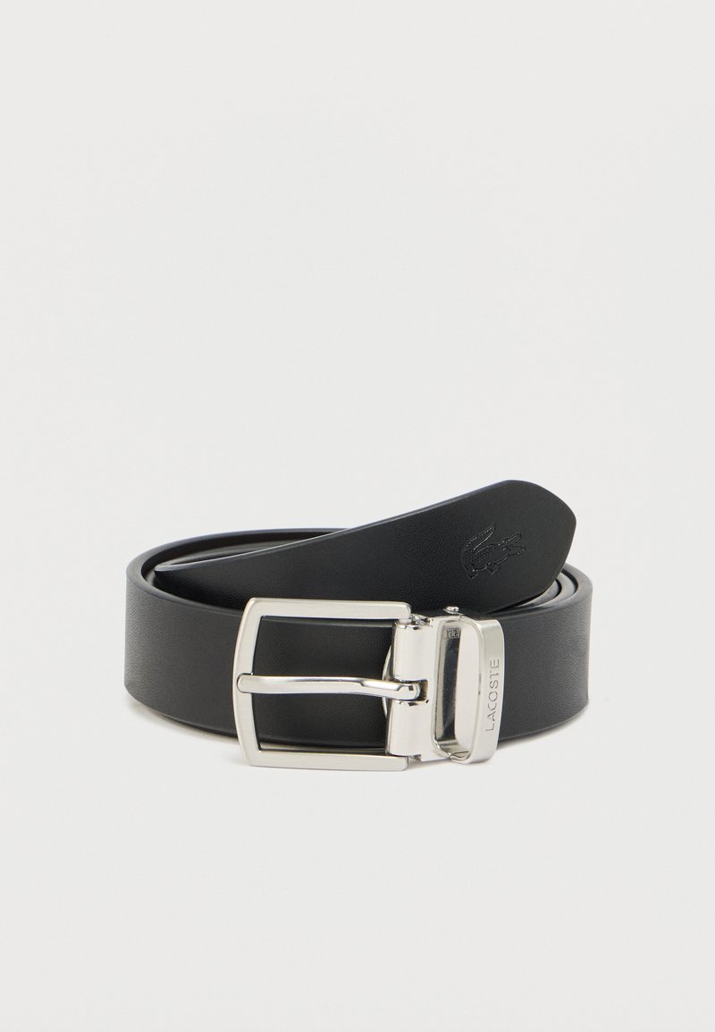 Ceinture en cuir noir avec une boucle rectangulaire argentée, présentant une texture lisse et un logo embossé sur la sangle, roulée à une extrémité.