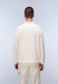 Pullover color crema in morbido tessuto con colletto e polsini a coste. Vestibilità rilassata con spalle scese, abbinato a pantaloni beige chiaro.