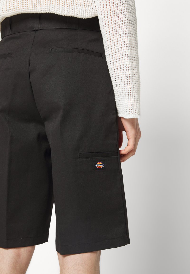 Black shorts made of sturdy fabric, featuring a back pocket and a small multi-color logo patch. Smooth texture with a tailored fit.