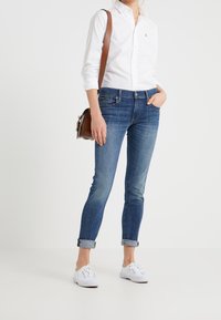 Skinny jeans i mellablå denim, något bleknade, med klassisk femficksdesign. Bärs med en vit knäppskjorta och vita sneakers.