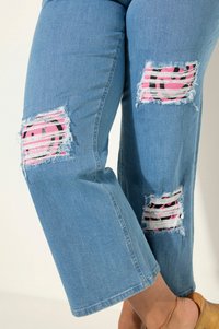 Ljust blå denimjeans med stora slitna lappar med ett rosa smiley-ansikte och ett svart randigt mönster. Ankellång med avslappnad passform.