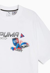 Vit t-shirt med korta ärmar som har PUMA-logotypen, färgglada klistermärken med biltema och en svart detalj vid halsringningen. Mjukt material, avslappnad passform.