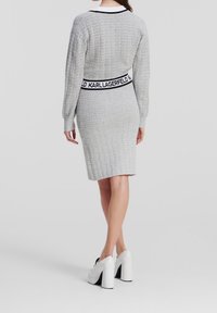 Szara dzianinowa sukienka o dopasowanym kroju, z długimi rękawami i kontrastującym czarnym paskiem w talii z napisem „KARL LAGERFELD”.