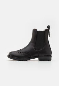 Botas Chelsea de cuero negro con paneles laterales elásticos, detalles de perforaciones, punta redondeada y una lengüeta en la parte trasera. Suela de goma texturizada.
