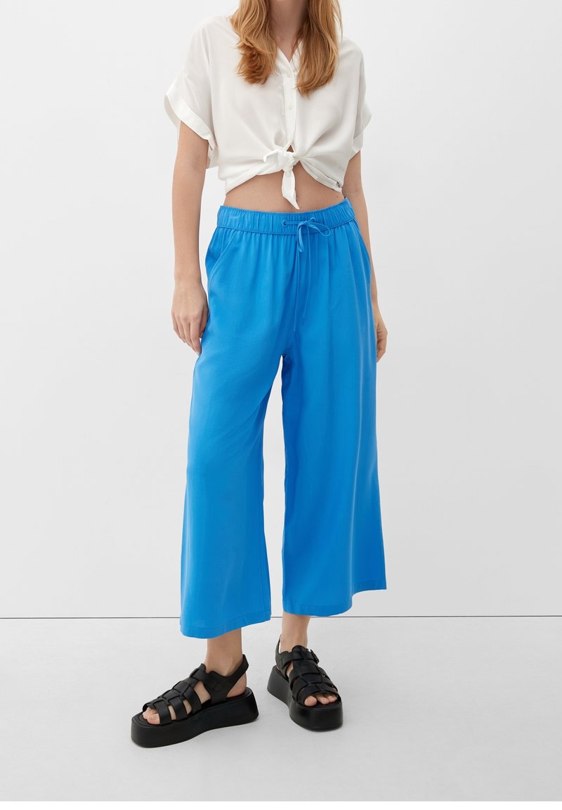 Lichtgewicht, cropped wit shirt gestrikt in de taille, gecombineerd met levendige blauwe wijde broekspijpen. Zwarte plateau sandalen maken de look compleet.