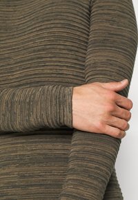 Langärmliges Oberteil in Brauntönen und Olivgrün, mit strukturierten horizontalen Streifen. Der Stoff ist weich und hat ein figurbetontes Design, das Unterarm und Hand zeigt.