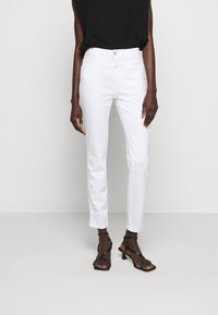 Pantalones de mezclilla blancos de corte recto con una cintura de altura media y diseño de cinco bolsillos, combinados con una blusa sin mangas negra y tacones negros con tiras.