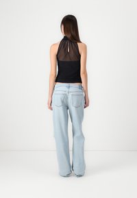Black halter top with sheer back detail, paired with light blue wide-leg denim jeans featuring a faded texture and back pockets.