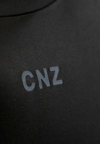 Schwarzer Stoff mit glatter Textur und subtilem Glanz; "CNZ"-Logo in kontrastierendem, mattgrauem Farbton, auffällig positioniert.