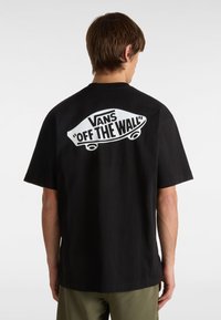 T-shirt in cotone nera con una grande grafica bianca "VANS 'OFF THE WALL'" sul retro, maniche corte e una vestibilità classica.