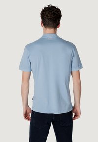 Polo shirt azzurro chiaro a maniche corte, con colletto, texture sottile e dettagli in rosso e bianco a contrasto sul collo posteriore.