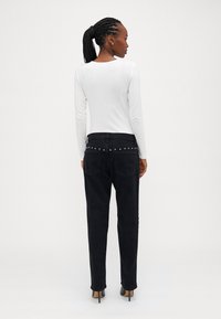 Cămașă albă cu mânecă lungă asociată cu blugi negri, având tivul din spate decorat cu bumbi argintii și croi skinny drept. Tocurile sunt accentuate.