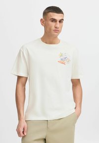 Cremefarvet bomulds t-shirt med korte ærmer, rund halsudskæring og en grafisk lomme på forsiden med frugter og tekst. Glat tekstur.