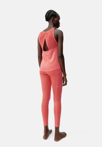 Roza športna obleka, ki vključuje brezrokavni top z izrezom na hrbtu in usklajene leggins hlače, izdelane iz lahke, raztegljive tkanine.