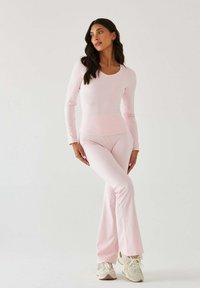 Jasnoróżowy top z długim rękawem i dopasowane rozkloszowane spodnie z elastycznego materiału, noszone z beżowymi butami sportowymi, tworząc skoordynowany strój.