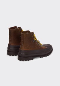 Stivali da trekking in pelle marrone con puntale in gomma marrone, lacci gialli e suola nera robusta. Presentano cuciture e dettaglio del logo sul lato.