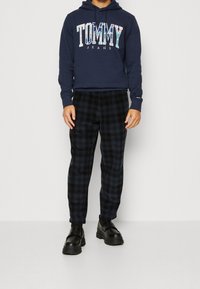 Sudadera navy con el logo de "TOMMY JEANS", combinada con pantalones de cuadros negros y mocasines negros de suela texturizada.