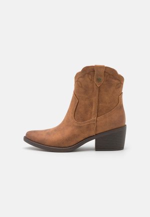 Botte style western mi-mollet en daim marron avec petit talon bloc, couture décorative et languette de tirage sur fond blanc.