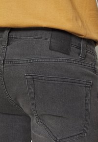 Grijze denim jeans met een klassiek vijf-pocketdesign, subtiele stiksels en een zwart leren logo-patch op de tailleband.