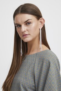 De longues boucles d'oreilles en argent avec des chaînes texturées, complétées par un haut gris à motif géométrique avec une coupe ample.