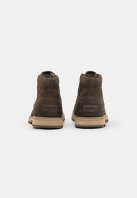 Botas de tobillo de ante marrón con suela de goma beige; cuentan con una etiqueta de marca en el talón y una textura suave con punta redonda.