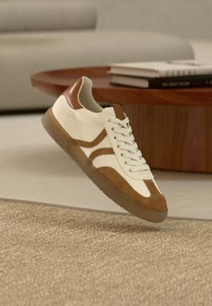 Λευκά και καφέ sneakers με υλικά από δέρμα και σουέτ, στρογγυλή μύτη, σύστημα κορδονιών και υφή στη σόλα από καουτσούκ με διακοσμητικές ρίγες στο πλάι.