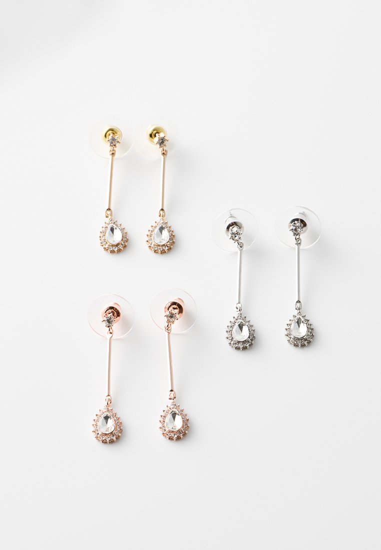 Tre paia di orecchini a goccia con pietre di forma goccia trasparenti circondate da pietre più piccole, in finiture dorata, argentata e rosa.