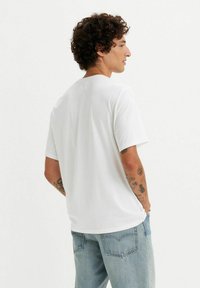 Camiseta blanca de manga corta con un ajuste relajado y cuello redondo, mostrada desde la parte trasera, combinada con jeans de mezclilla azul claro.