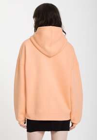 Brzoskwiniowy, oversize'owy hoodie o miękkiej fakturze, z kapturem na sznurkach i prążkowanymi mankietami, połączony z czarną dżinsową spódniczką mini.