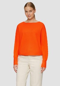 Oranger gerippter Pullover mit weitem Ausschnitt und langen Ärmeln. Kombiniert mit cremefarbenen Hosen. Strukturiertes Stoff sorgt für Dimension.