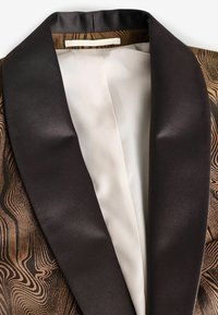 Chaqueta de esmoquin que presenta un tejido marrón texturizado con patrones en espiral, una solapa de satén negro y un forro de seda blanca.