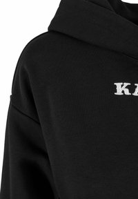 Mustmust koos tekstureeritud kangaga, millel on valge tikandiga logo. Kapuutsil on topeltkiht, mis rõhutab mugavust.
