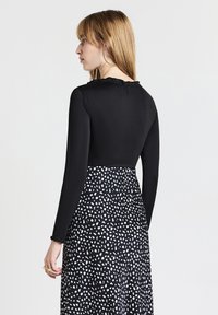Maglietta nera a maniche lunghe con colletto arricciato abbinata a un vestito con motivo a pois bianco e nero. Texture liscia, parte superiore aderente.