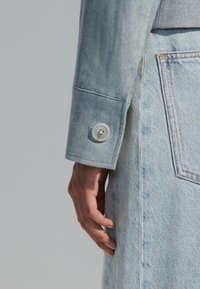 Hele hall denim jope, millel on kalasabamuster, valge nööp mansetil ja heledat värvi denim seelik, millel on nähtavad õmblused.