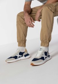 Mornarsko plave i sive tenisice s bijelim naglascima, mrežastim i antilop materijalima, okrugli vrh i gumeni potplat, uparene s bež sužavajućim hlačama i bijelim čarapama.